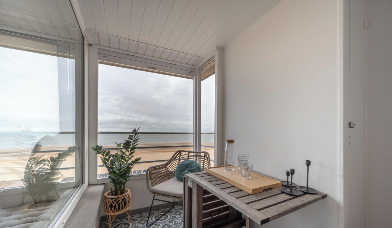 Un balcon avec vue sur la mer, une chaise en osier, une petite table avec des verres et une plante en pot.