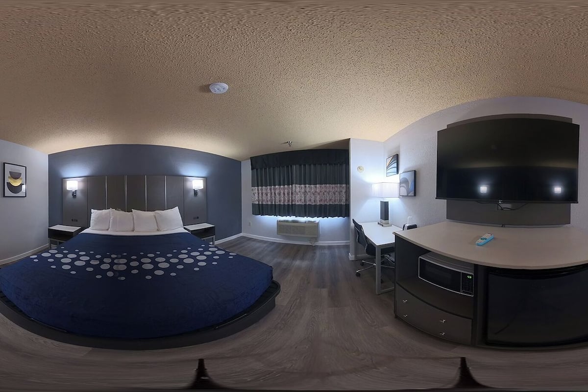 Une chambre d’hôtel moderne dotée d’un lit aux lignes courbes, d’un bureau, d’un téléviseur à écran plat et d’une grande fenêtre avec des rideaux.