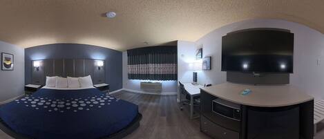 A modern hotel room with a curved bed, a desk, a flat-screen TV, and a large window with curtains.