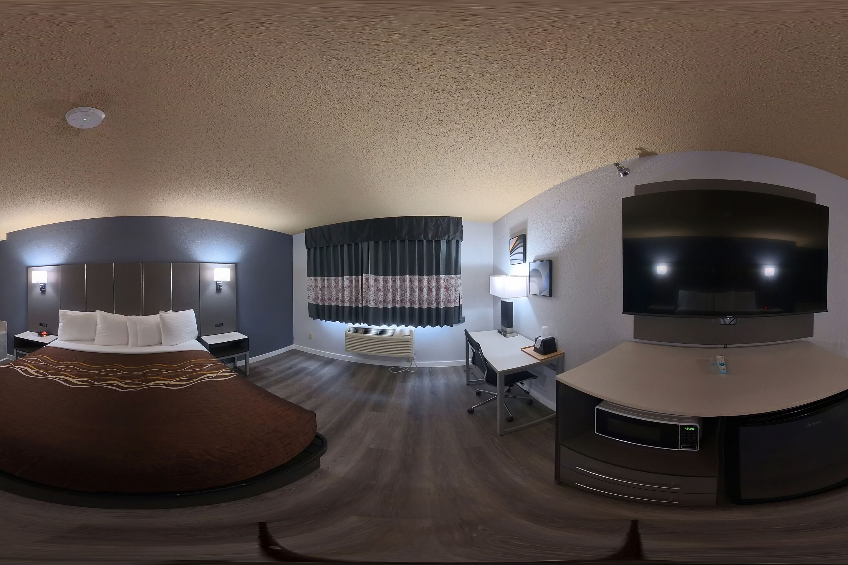 A modern hotel room with a large bed, a desk, a TV, and a ceiling-mounted air conditioning unit.