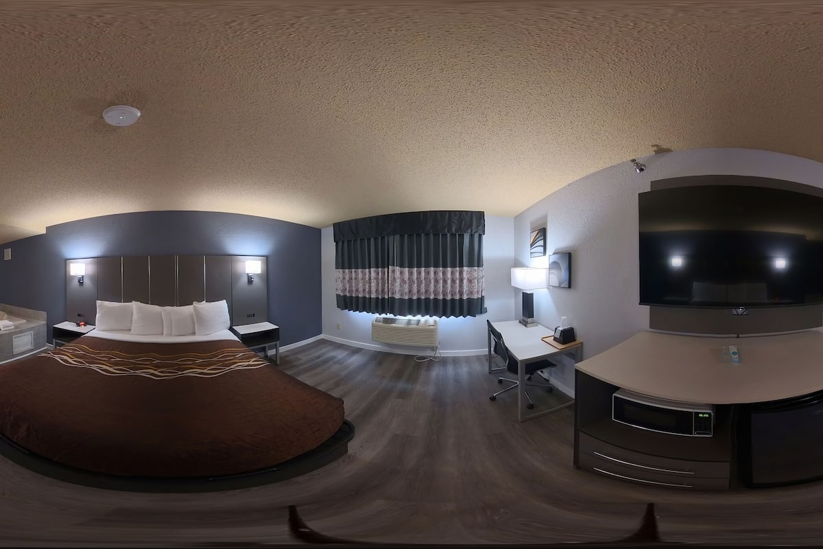Une chambre d’hôtel moderne dotée d’un lit king-size, d’un bureau, d’une télévision à écran plat et d’un coin salon avec un canapé et des rideaux.