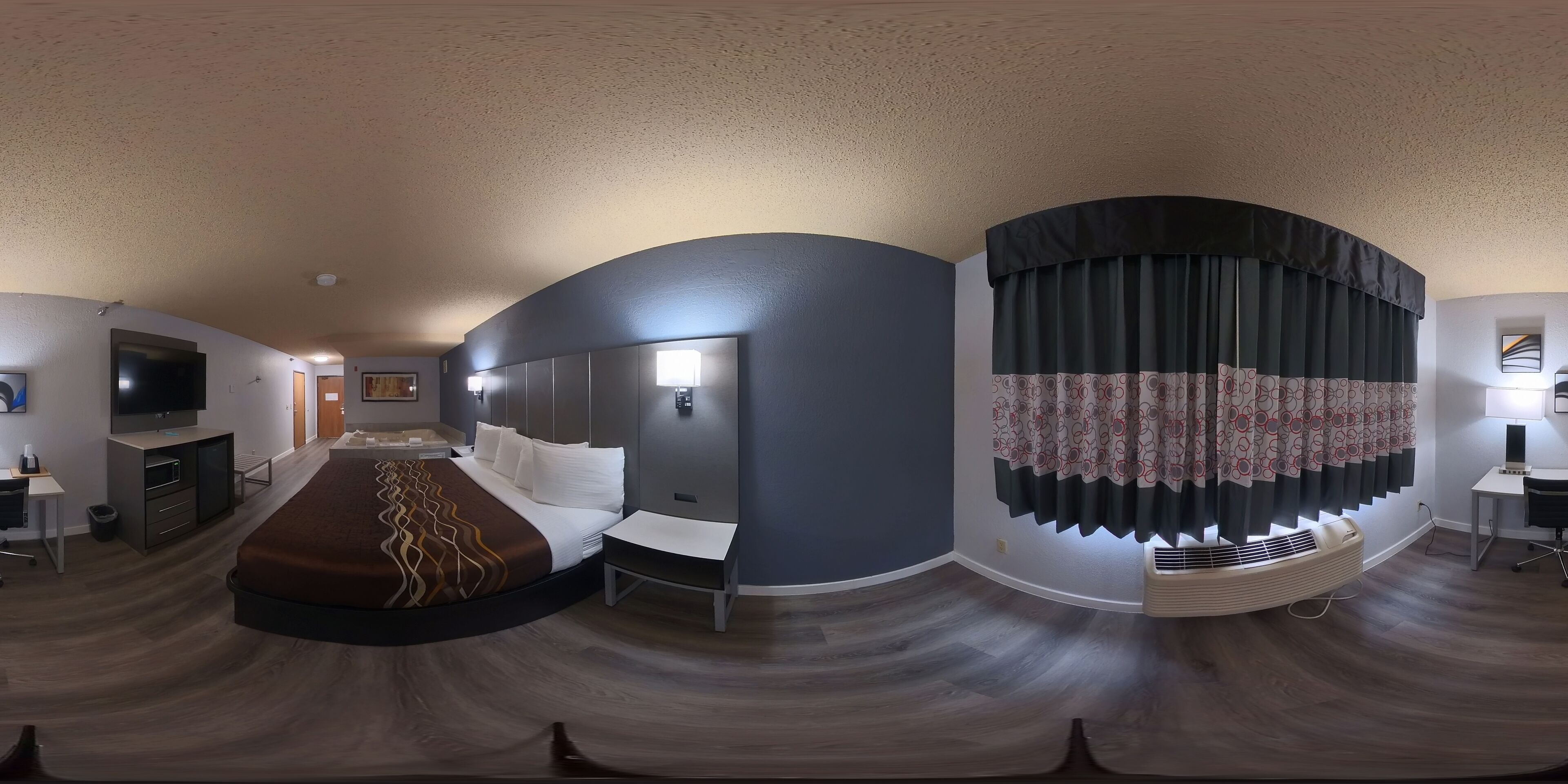 A modern hotel room with a curved ceiling, a large bed, a desk, a television, and a window with curtains.