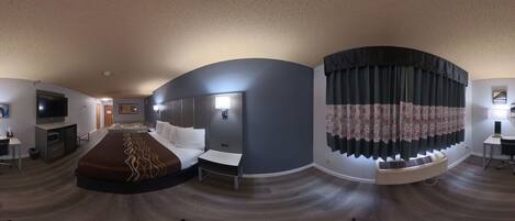 A modern hotel room with a curved ceiling, a large bed, a desk, a television, and a window with curtains.