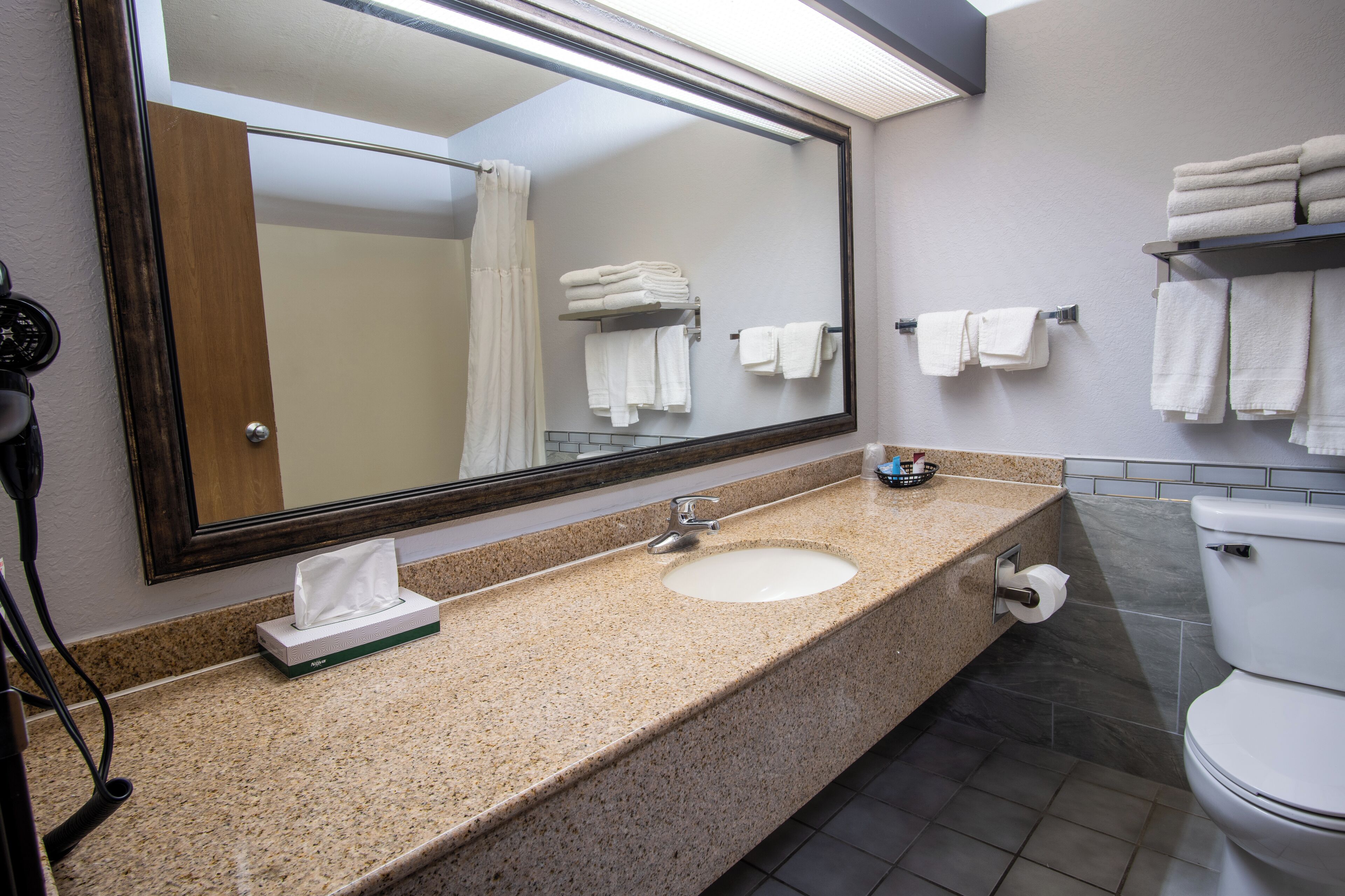 Un baño con lavamanos, espejo, toallero y retrete.