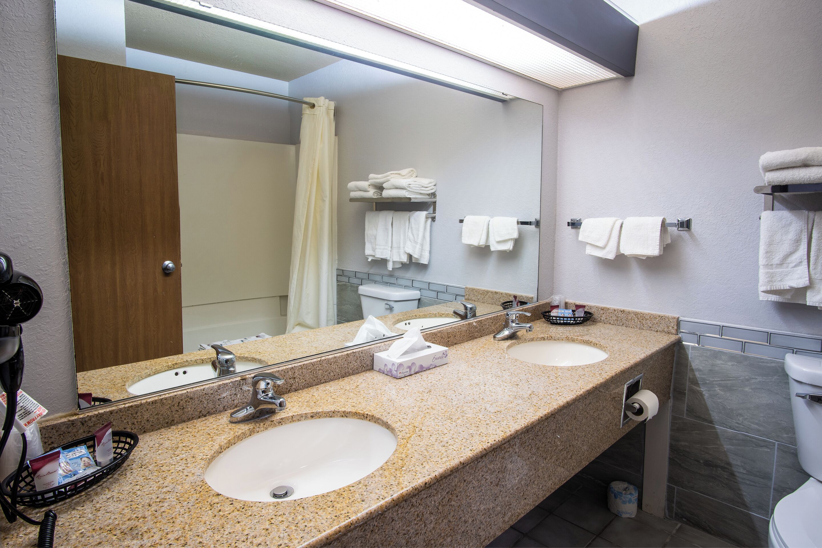 Une salle de bain d’hôtel avec deux lavabos, un grand miroir et un espace douche.