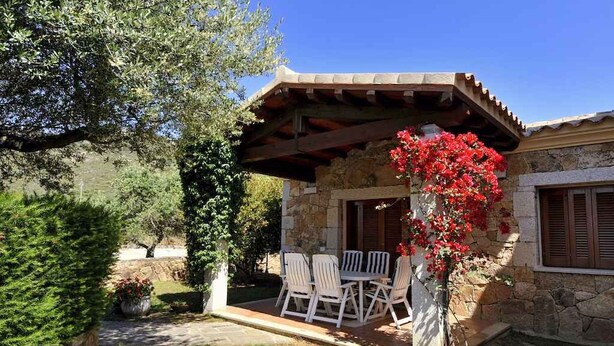Un edificio de piedra con un patio cubierto, asientos al aire libre y una maceta con flores rojas.