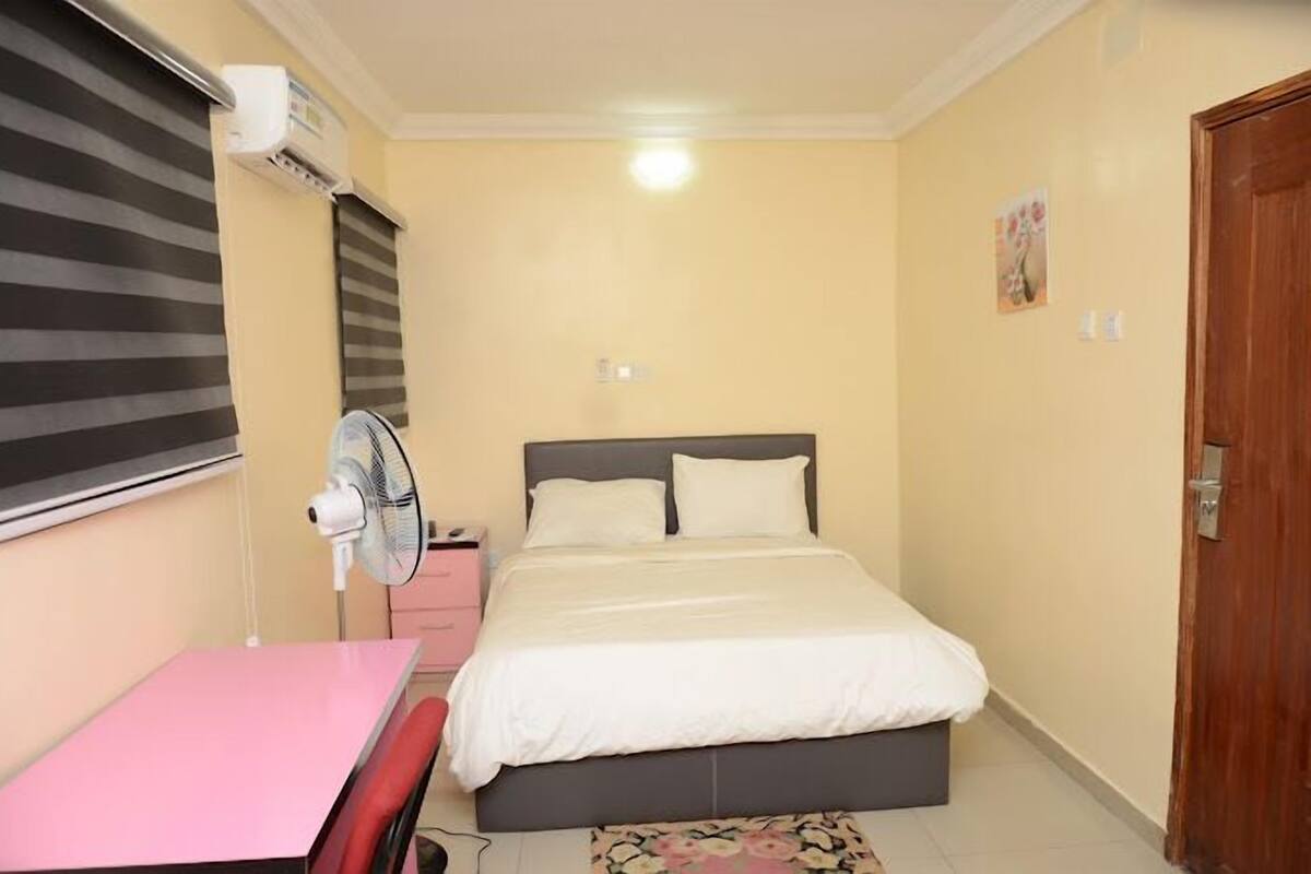 A bedroom with a bed, a desk, a chair, an air conditioner, and a door.
