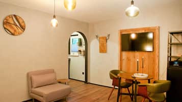 A cozy room with a sofa, a round table with chairs, a wooden wall decoration, and a clock.