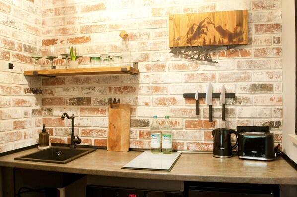 A kitchen with a brick wall, a wooden shelf, a knife rack, a coffee maker, and a digital clock.