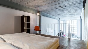 Un dormitorio con una cama grande, piso de madera, una estantería y una silla.