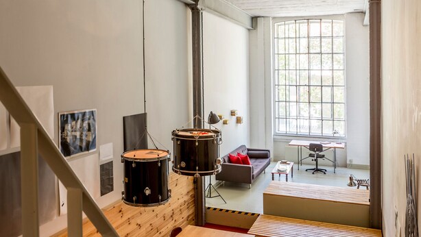 Un espacio habitable moderno con una escalera, un set de batería, un sofá y un ventanal grande.