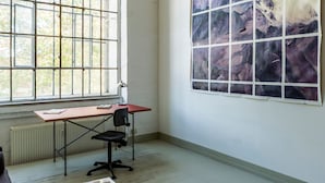 Una habitación con un ventanal grande, un escritorio con silla y un cuadro abstracto de grandes dimensiones en la pared.