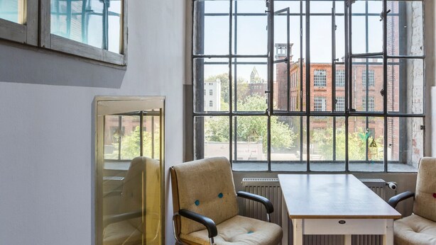 Una habitación con un ventanal grande, dos sillas, una mesa y un radiador.