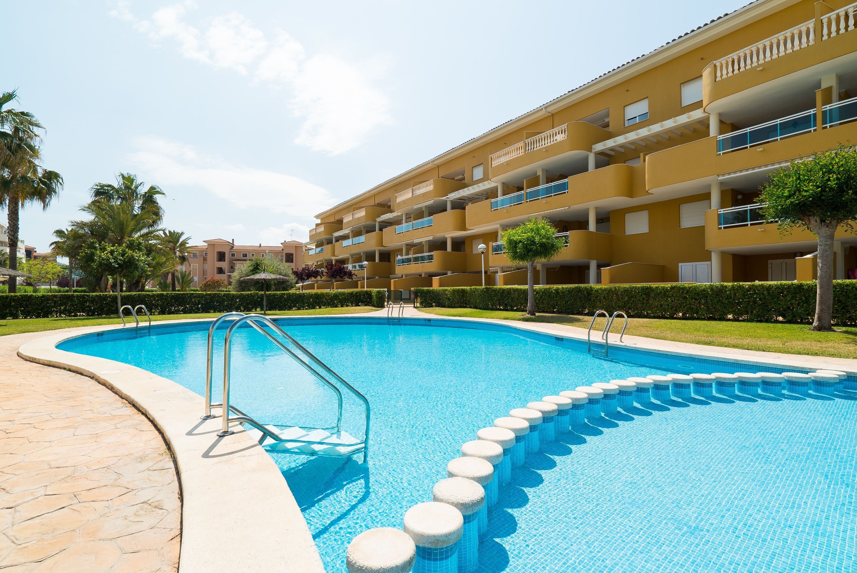 A swimming pool with a tiled edge, a metal ladder, and a series of circular steps leading into the water.
