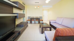 Een moderne woonkamer met een flatscreen televisie, een bank, een eettafel met stoelen en hanglampen.