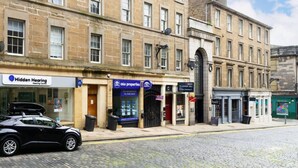 A street view with a row of buildings, including a hearing center, a property agency, and a hair salon. - Castle Street Apartment - stylish city centre pad (Dundee)