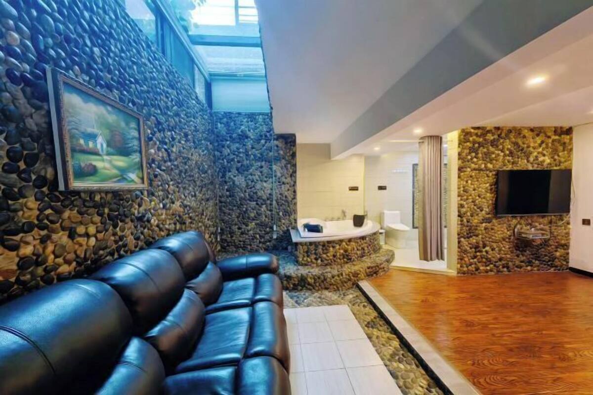 Ein modernes Interieur mit einer Steinwand, einer schwarzen Ledersofa, einem Steinkamin und einem an der Wand montierten Fernseher.