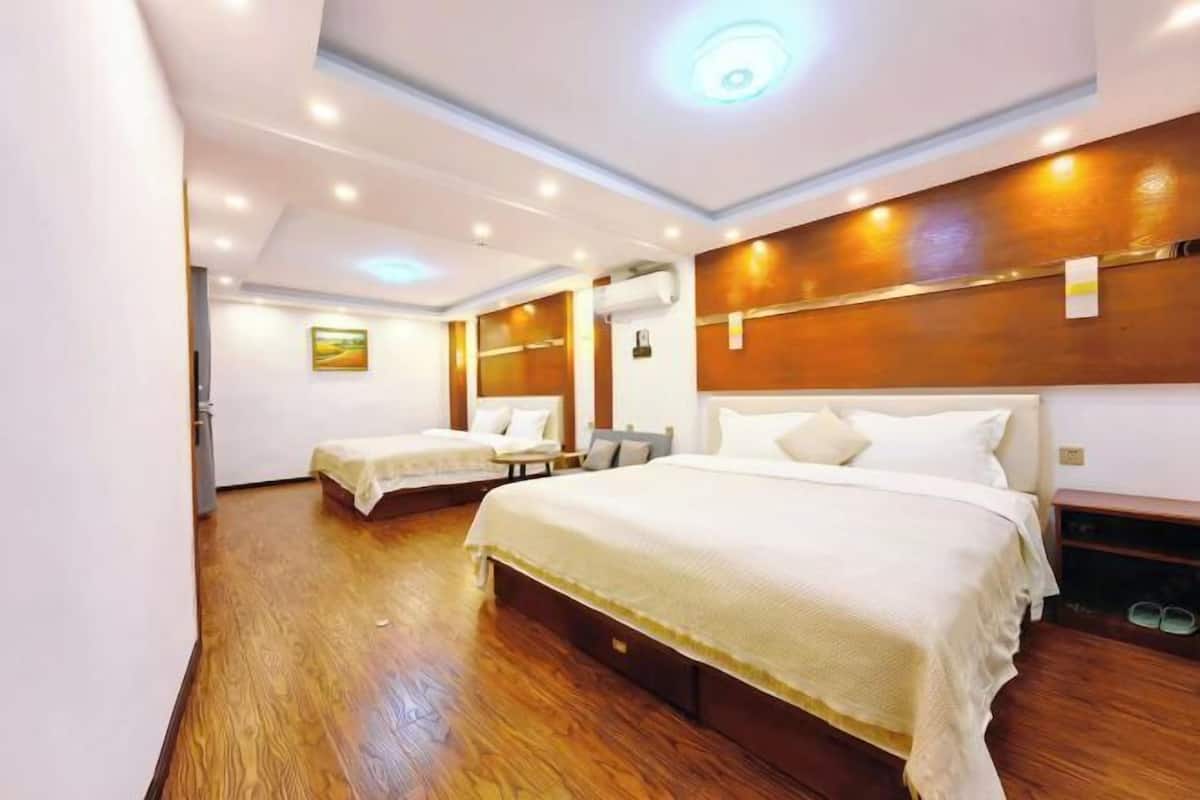 Ein Hotelzimmer mit zwei Betten, Holzboden, einer Decke mit integrierter Beleuchtung und einer Wand-Klimaanlage.