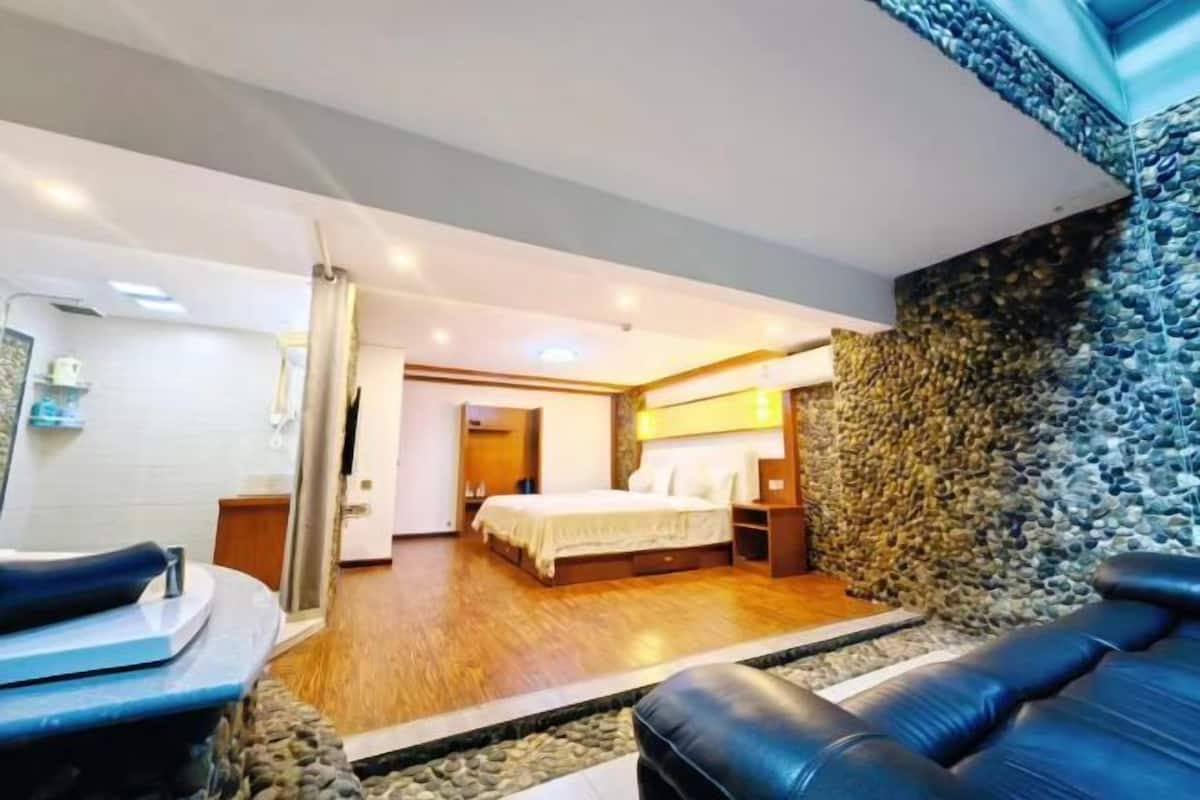 Ein modernes Hotelzimmer mit Bett, einer Sitzecke mit Massagesessel, einer Steinwand und Holzboden.
