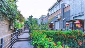 Une ruelle étroite avec un escalier menant à un immeuble, le tout étant entouré d’une végétation luxuriante et de plantes en fleurs.
