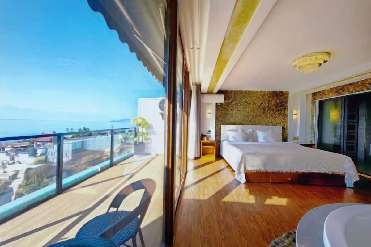 Ein Schlafzimmer mit einem großen Bett, einem Balkon mit Stuhl und Blick aufs Meer.