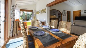 A dining area with a wooden table set for four, surrounded by wicker chairs, with a view of the garden through the open door. - Casa Lea in Alcanal (Alcalali)