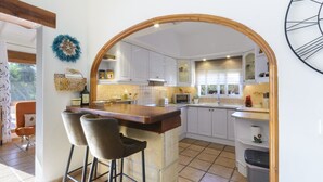 A kitchen with white cabinets, a wooden island with bar stools, a microwave, and a trash bin. - Casa Lea in Alcanal (Alcalali)