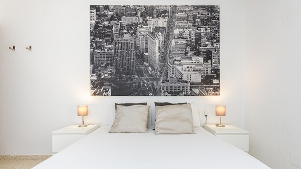 A bedroom with a large bed, two bedside tables with lamps, and a cityscape artwork on the wall.