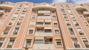 A multi-story building with balconies, air conditioning units, and a clear sky.