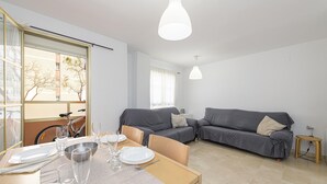 A modern living room with a dining area, grey sofas, and a bicycle in the background.