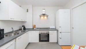 A modern kitchen with white cabinets, a built-in oven, a toaster, and a refrigerator.