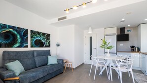 Uma sala de estar moderna com um sofá cinzento, uma mesa de jantar com cadeiras brancas e arte abstrata nas paredes.