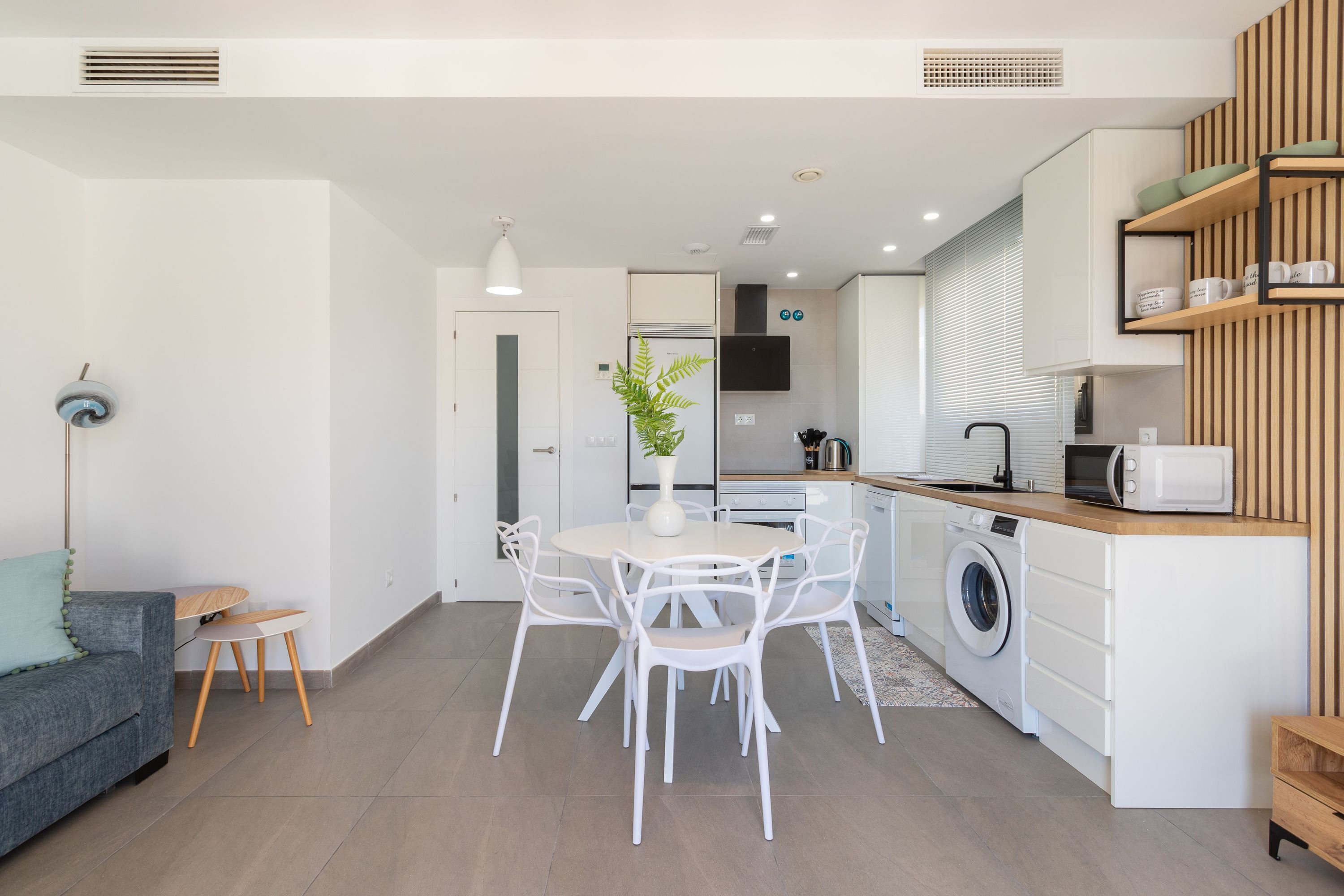 Una cocina moderna con electrodomésticos blancos, una zona de comedor con una mesa redonda y sillas, y un área de lavandería con lavadora.