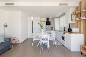 A modern kitchen with white appliances, a dining area with a round table and chairs, and a laundry area with a washing machine. - La Biznaga in Costa del Sol (Fuengirola)