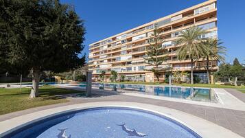 Un hotel de varios pisos con balcones, piscina con mosaicos de delfines y una palmera.