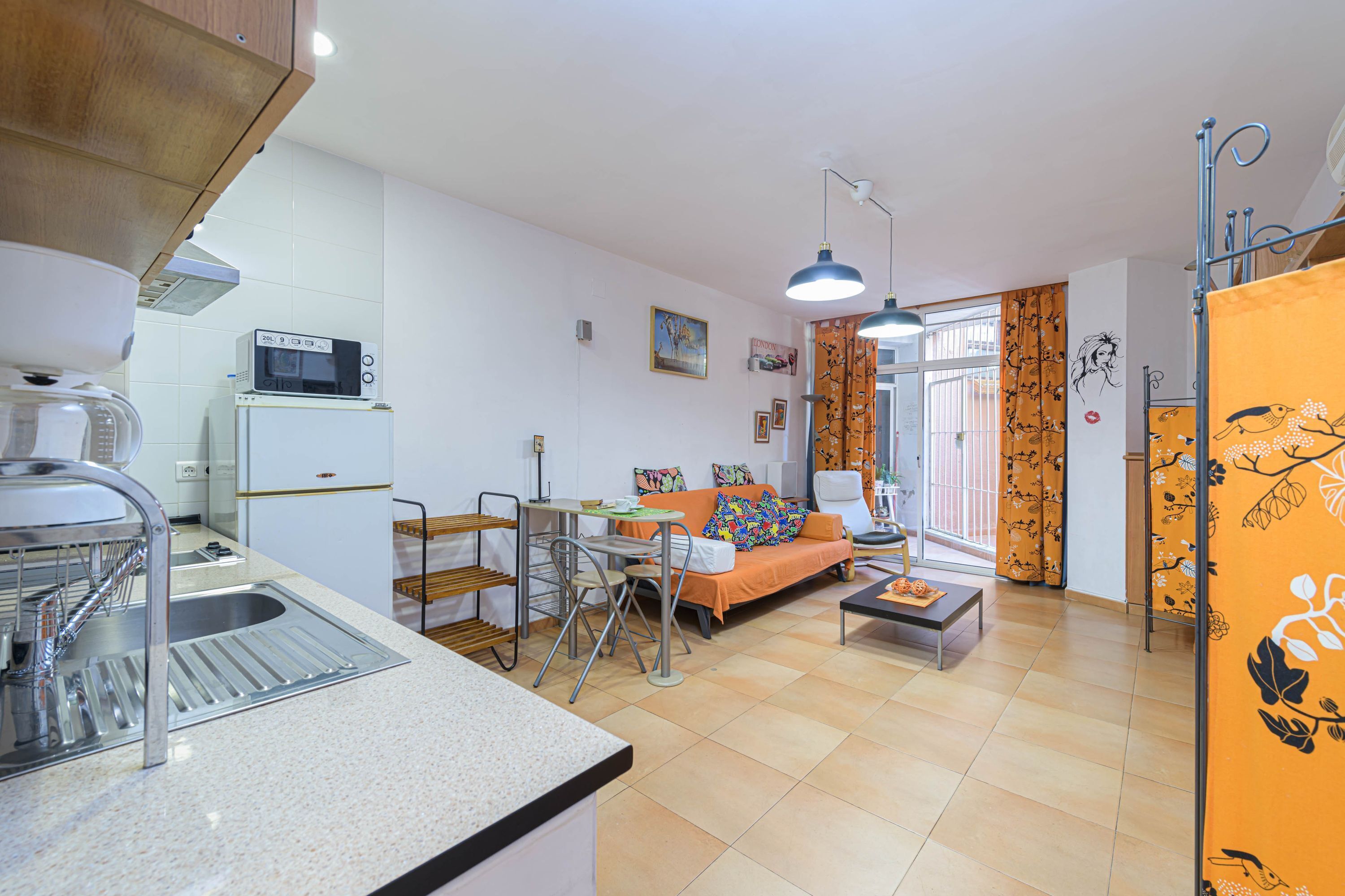 Un espacio habitable compacto con kitchenette, zona de comedor y área de estar con sofá y mesa de centro.