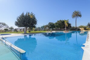 A clear blue swimming pool with a palm tree and a tall tree in the background. - Estudio La Colina in Torremolinos (Torremolinos)