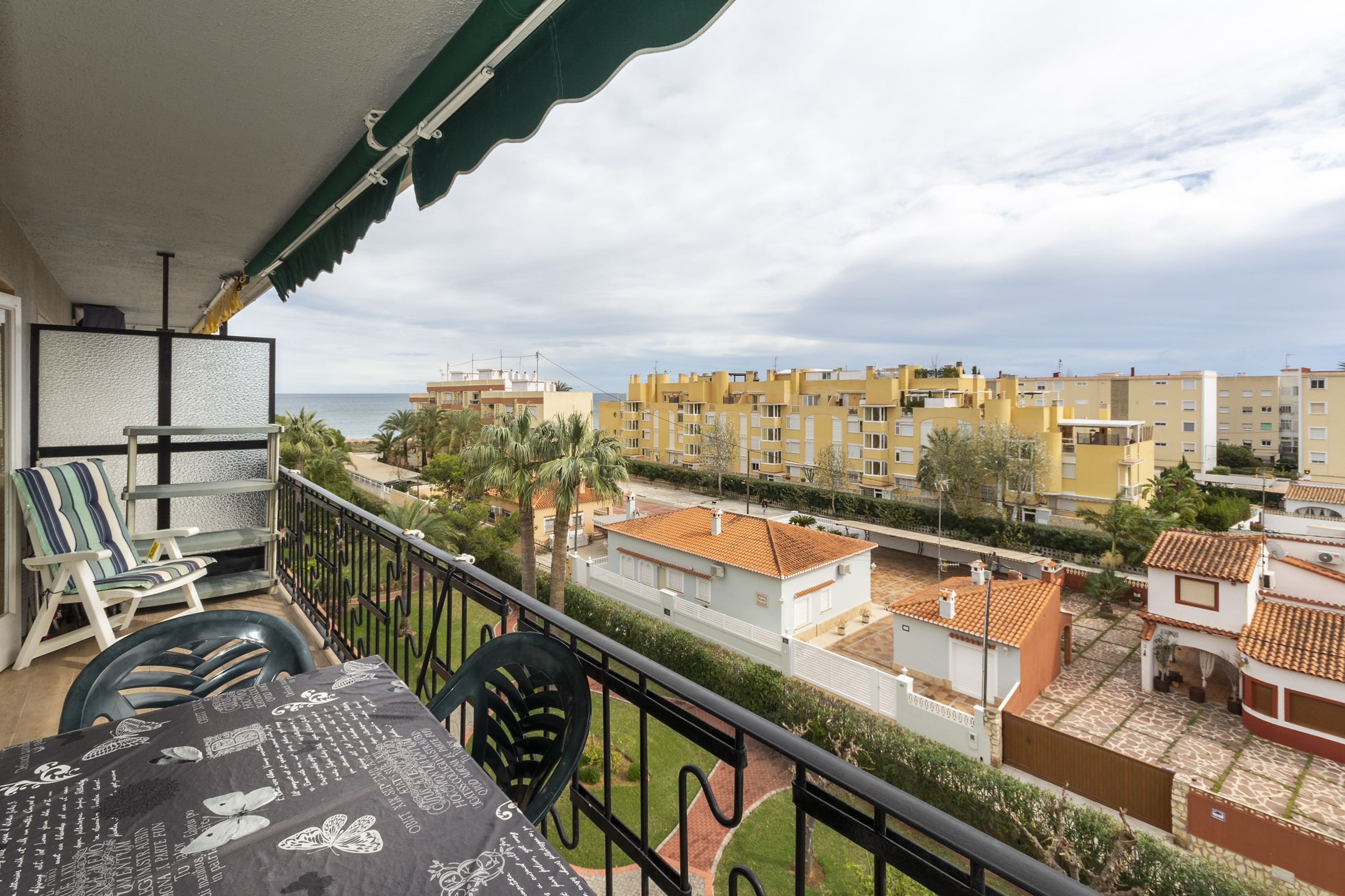 En balkon med et bord og stole, med udsigt over et boligområde med bygninger og en klar himmel.