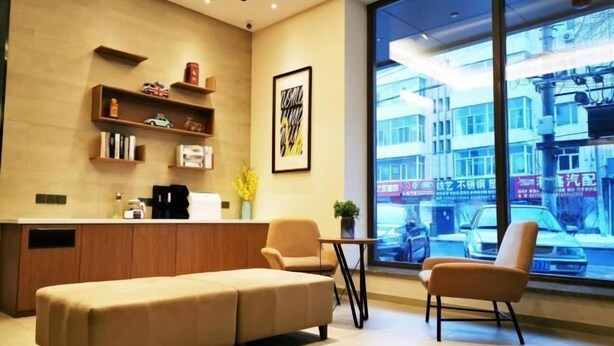 A modern reception area with a sofa, chairs, a coffee machine, and a counter with shelves. - HanTing Hotel (Harbin Exhibition Center Sports College) (Harbin)