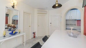 A modern kitchen with white cabinets, a white countertop, and a dining area with a white table and black chairs. - Arte De Luz in Urbanizaci n Riviera Sol (Mijas)