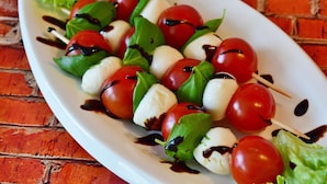 A plate of mozzarella and cherry tomatoes on skewers with basil leaves and a drizzle of balsamic glaze. - Residence Villa Giada Four-room Apartment 7 Persone Ibis (Imperia)