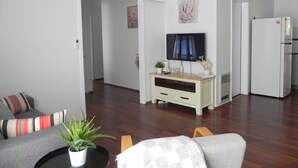 Ein modernes Wohnzimmer mit Fernseher, einer kleinen Kommode und einem Kühlschrank.