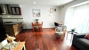 Ein modernes Wohnzimmer mit Holzboden, einer Essecke mit Tisch und Stühlen, einer Couch und einer Küchenzeile mit Herd und Schränken.