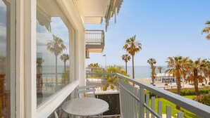 A balcony with a table and chairs, overlooking a beach with palm trees and a clear sky. - Garceta in Benalmadena (Benalmádena)