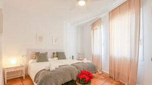 A bedroom with two beds, a nightstand, a ceiling fan, and a potted plant. - Casa Rural Los Menestrales (Lora Del Rio)