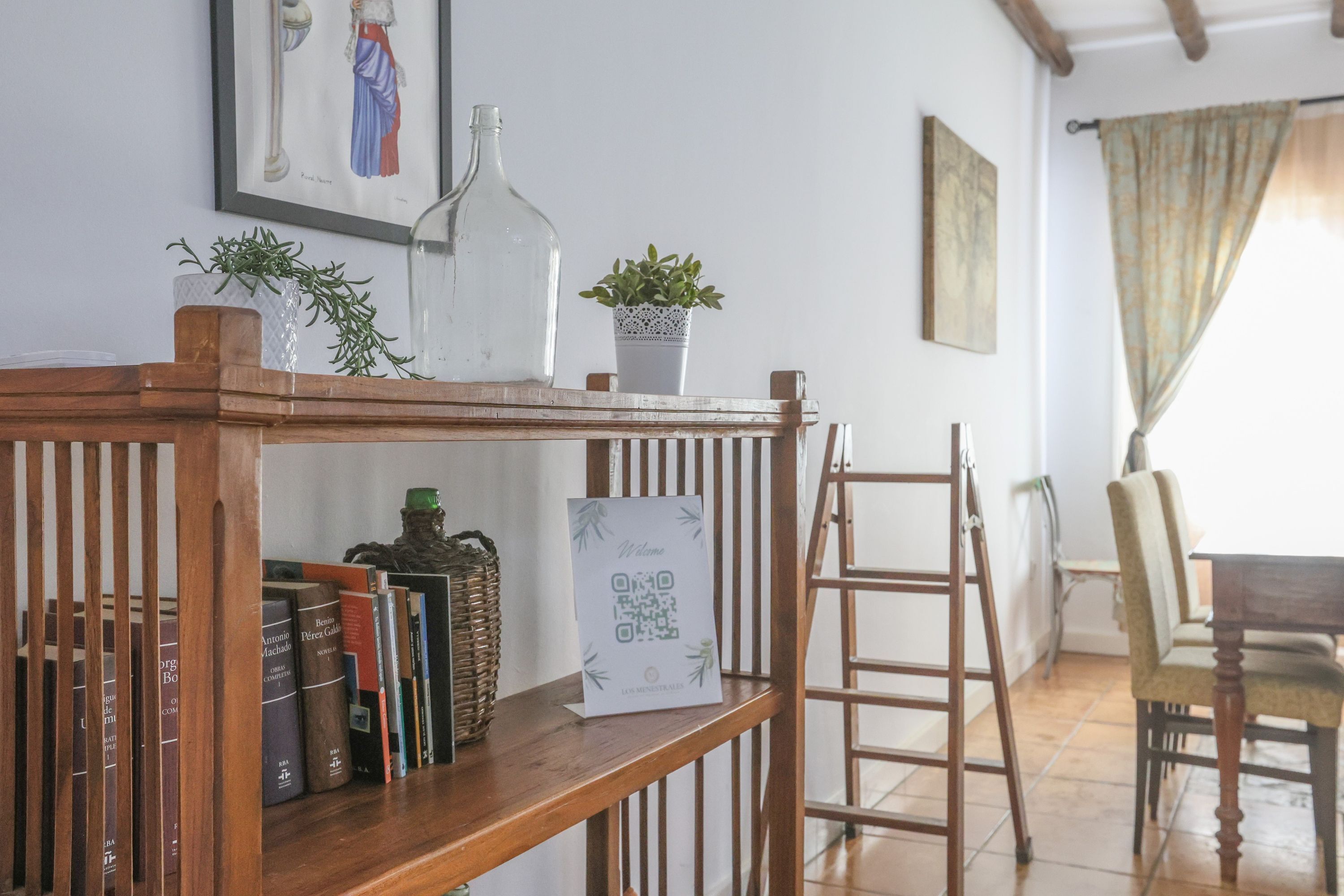 A wooden shelf with books, a QR code sign, a potted plant, and a ladder. - Casa Rural Los Menestrales (Lora Del Rio)