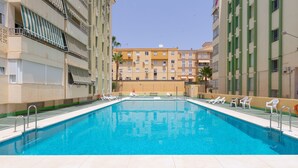 Una piscina con lettini e vista su un edificio a più piani sullo sfondo.