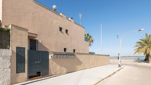 A building with a beige facade, a gated entrance, and a clear view of the sea.