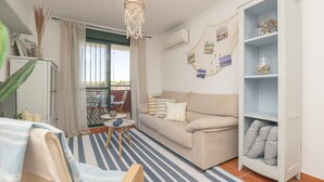 A living room with a sofa, a chandelier, a bookshelf, and a view of the outside. - Marina Place in Chiclana de la Frontera (Chiclana de la Frontera)