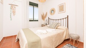 A bedroom with a bed, a bedside table, a hanging light fixture, and a window. - Marina Place in Chiclana de la Frontera (Chiclana de la Frontera)